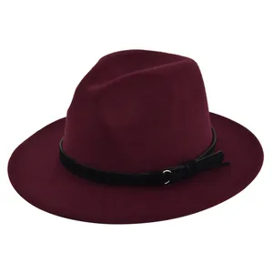 Detail of burgundy wool fedora hat featuring black band with gold ring and tassel decoration