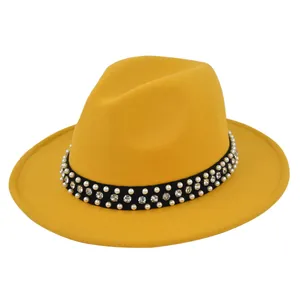 Close-up of mustard yellow fedora hat featuring black band with pearls and rhinestones