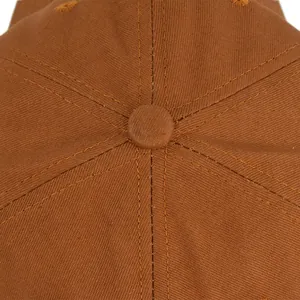 Makro-Detail einer braunen Baseballkappe mit gelben Kontrastnähten und stoffbezogenem Knopf