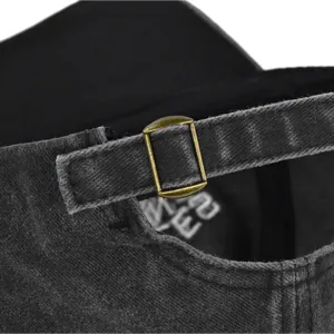 Detail view of the bronze metal adjustable buckle and denim strap on a dark grey vintage cap