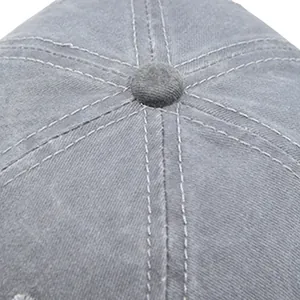 Détail macro d'une casquette en coton gris lavé montrant le bouton et les doubles coutures