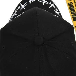 Detail view of black baseball cap with white graffiti brim and yellow warning strap