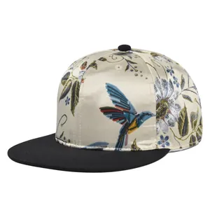 Close-up of intricate hummingbird and floral embroidery on champagne satin snapback cap