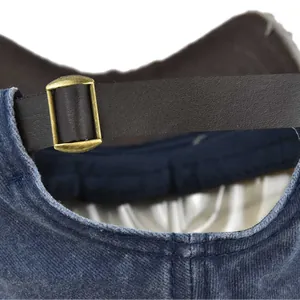 Detail of vintage washed denim baseball cap with leather strap and brass metal buckle