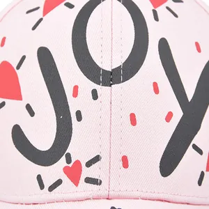 Close-up of pink cotton twill baseball cap showing black JOY print and red heart detail