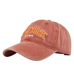 Detailed close-up of orange 3D New York embroidery on washed brick red cotton baseball cap