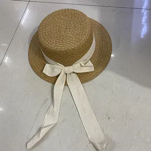 Detail of raffia straw boater hat with cream herringbone ribbon and bow tie