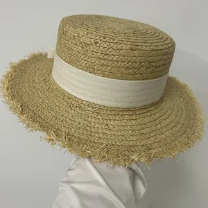 Detail of flat-top raffia sun hat featuring white ribbon and frayed brim edges