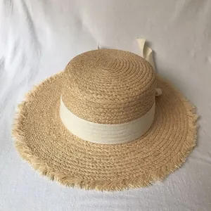 Close-up of a flat top raffia sun hat showing textured weave and raw fringe brim