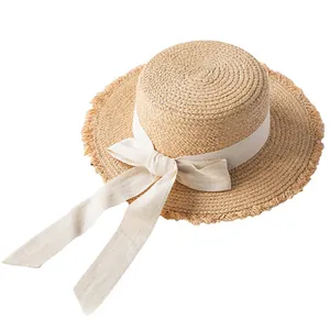 Detail of raffia straw hat featuring a beige bow ribbon and frayed edge brim design