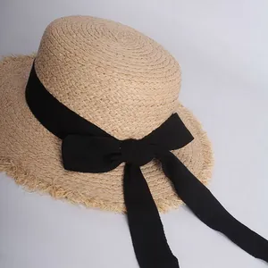 Detail of raffia straw sun hat featuring a black ribbon bow and stylish fringed brim edges