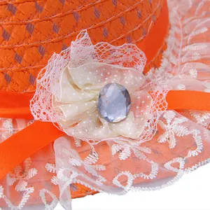 Detailed close-up of orange straw hat featuring white lace trim and a jewel bow