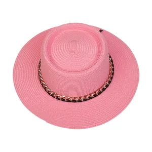 Detail eines rosa Strohhutes mit roségoldener Metallkette und schwarzem Lederband
