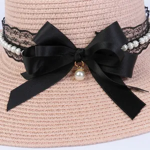 Detailed close-up of straw hat featuring black lace, white pearls, and a satin bow