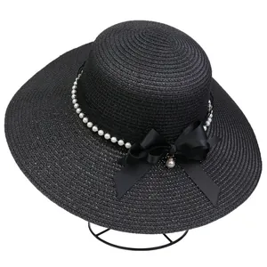 Detailed view of black straw hat with white pearl beads and elegant satin bow