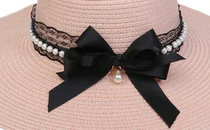Detail of pink straw hat featuring black lace ribbon, pearl beads and large bow ornament