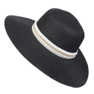 Detail of black straw sun hat with white ribbon, faux pearls and gold chain accent