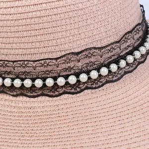 Detail of pink straw hat featuring black lace ribbon and elegant white pearls
