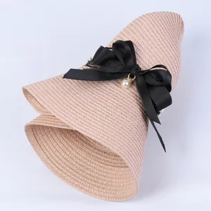 Detail of pink woven sun hat featuring a large black bow and elegant pearl pendant accent