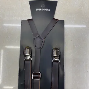 Detail view of brown Y-shape leather suspenders with metal clips on branded packaging