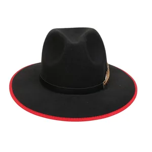 Dettaglio del fedora di lana nera con piuma dorata e bordo cucito in rosso acceso