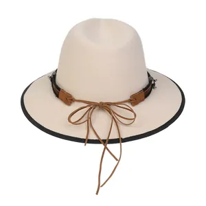 Dettaglio di cappello fedora beige con fascia in pelle marrone, fiocco e borchie in metallo