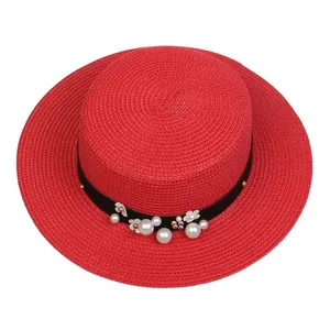 Detail of red straw hat featuring black ribbon with white pearls and floral decorations