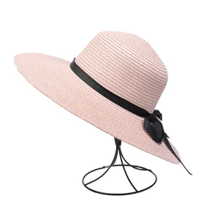 Detail of pink wide brim straw hat with black ribbon bow on a minimalist display stand