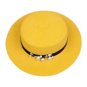 Detail of yellow flat top straw hat featuring black ribbon with pearls and white flowers
