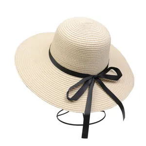 Detail of beige straw hat with black grosgrain ribbon bow on a minimal display stand