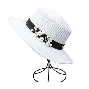 Close-up of white woven straw hat with black grosgrain ribbon, pearls and floral details