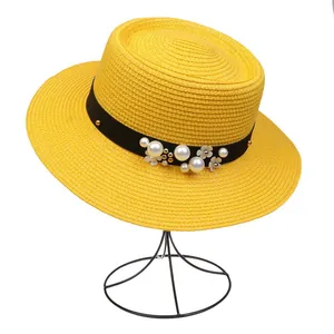 Detail of yellow straw hat with pearl accents, floral decor, and black ribbon band