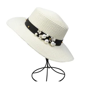Close-up of beige straw hat with black ribbon, white pearls, and floral sequin embellishments