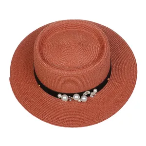 Detailed close-up of brick red straw hat with black ribbon, pearls and floral accents