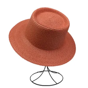 Detail view of brick red straw hat with elegant spiral weave texture on a black metal stand