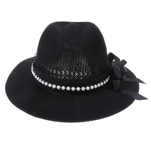 Detail of black straw fedora featuring white pearl beads and a satin ribbon bow