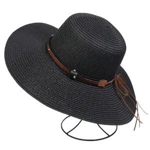 Detail of black straw sun hat with brown leather band, silver studs and tassel decor