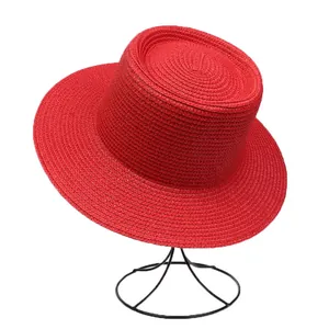 Detailed view of red straw boater hat with fine spiral woven texture on a stand