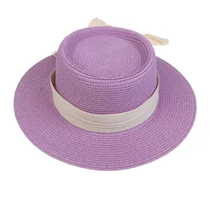 Close-up of a purple straw boater hat featuring a cream ribbon bow and fine woven texture