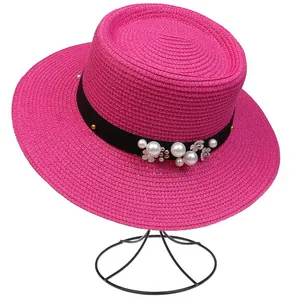 Detail of fuchsia straw hat featuring black ribbon with pearls and white floral ornaments