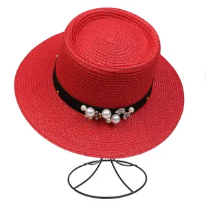 Close-up of red woven boater hat with black ribbon, white pearls, and gold metal flower detail