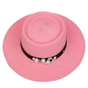 Detail of pink straw boater hat with black band, white pearls and floral accents