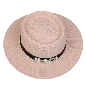 Close-up of pink straw hat with black ribbon, white pearls and floral decoration