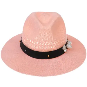 Close-up of pink straw hat with pearl accents, black ribbon, and floral decorations