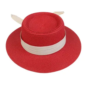 Detail of red straw boater hat with flat top and cream-colored fabric ribbon ties