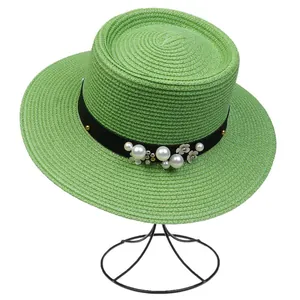 Detailed view of light green straw hat with pearl floral ribbon on plain background