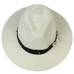Detail of cream straw hat featuring black ribbon with pearls, gold beads and a side flower