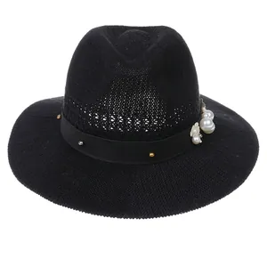 Detail of elegant black straw hat featuring pearl accents and metallic floral decoration