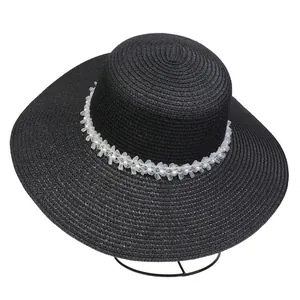 Close-up of black straw sun hat featuring white gauze floral and pearl trim detail