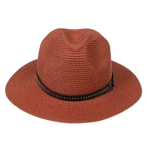 Macro shot of rust red Panama straw hat with black leather band and silver rivet details